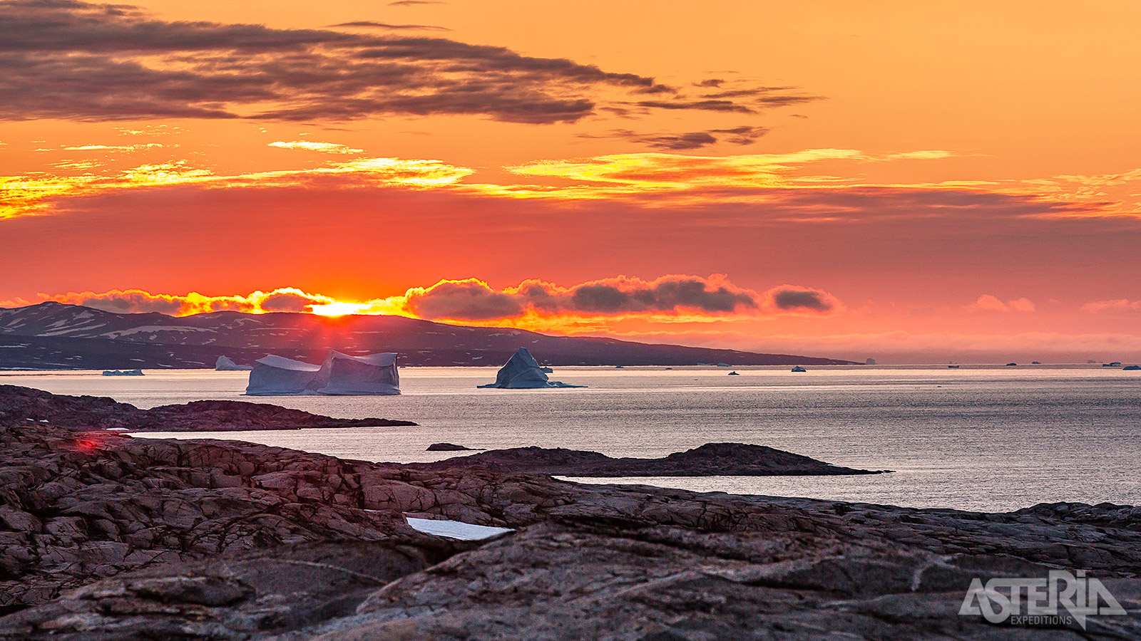 De zonsondergang itransformeert het landschap in een betoverend schouwspel van gouden en oranje tinten die de majestueuze ijsbergen en fjorden in een warme gloed hullen